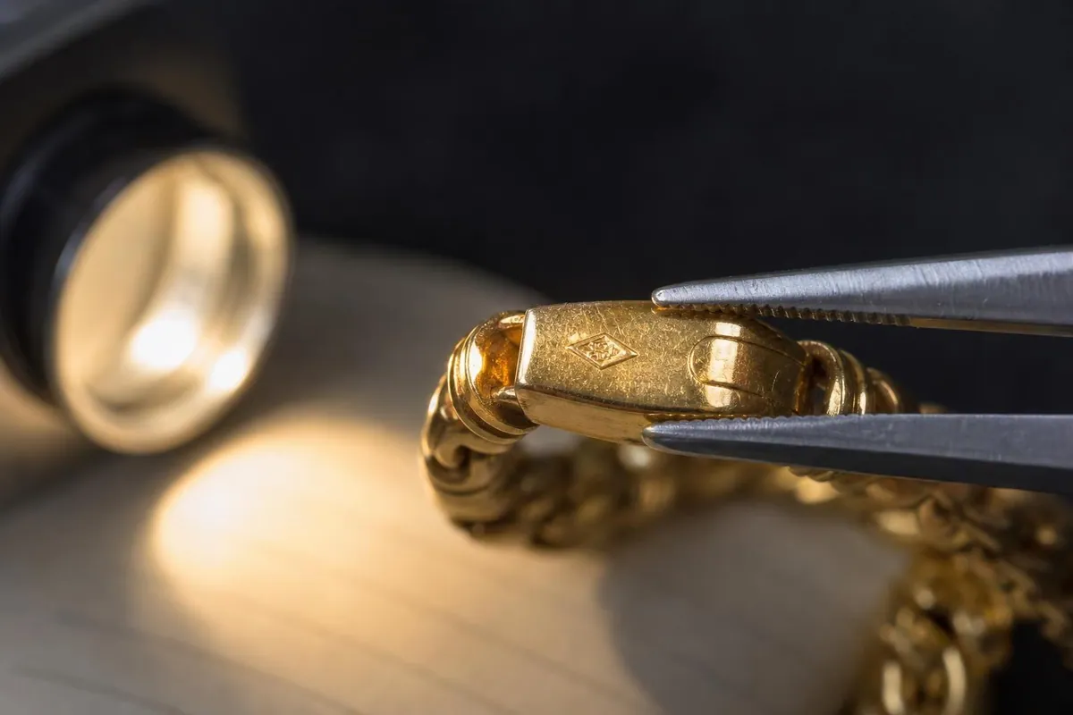 Vue macro du poinçon de garantie estampé sur le fermoir d’un bracelet en or tenu par une pince brucelles